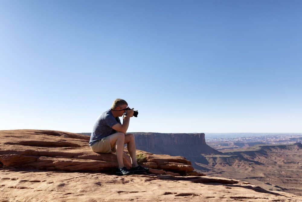 mature man taking photos of the grand canyon while sitting down